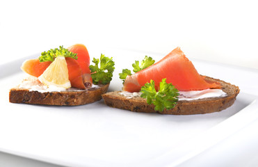 Two sandwiches with smoked salmon, sauce and parsley on a white background