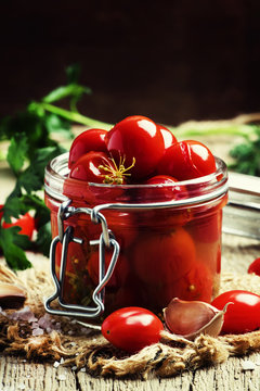 Marinated cherry tomatoes in a glass jar, vintage wooden backgro