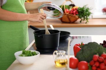 Young woman is cooking by the stove in the kitchen, close up.