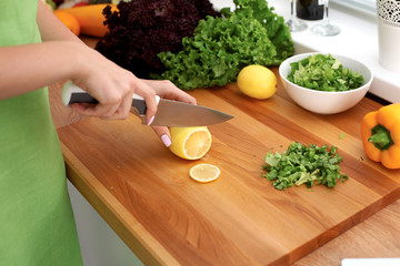 Closeup of woman hands cooking vegetables salad in kitchen. Housewife cuts lemon. Healthy meal and vegetarian concept.