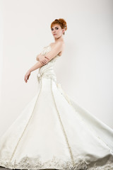 Fototapeta premium Beautiful young redhead bride wearing white wedding dress with professional make-up and hairstyle