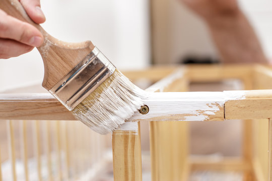 Man painting wood furniture with a brush and paints, close-up