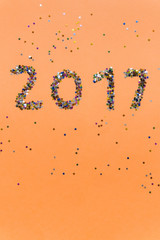 2017 made of multicolored confetti in the shape of stars on the orange background