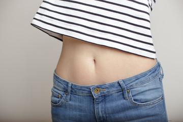 girl in blue jeans and a striped sweater and lifted her arms bared belly with a beautiful waist and umbilicus - obrazy, fototapety, plakaty