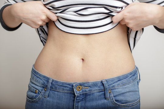 woman in blue jeans held up a striped sweater and bared belly with a beautiful waist and umbilicus