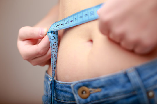 fair-skinned woman in blue jeans is measured using a tape beautiful slender waist