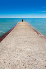 Fototapeta premium Osoba siedząca samotnie na stacji dokującej z jasnym błękitnym niebem