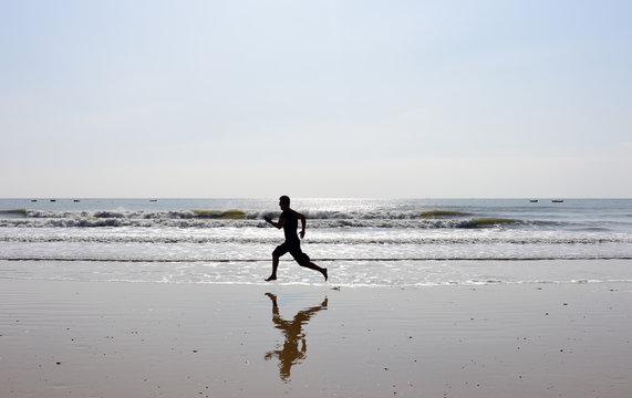 Man running on beach with sea waves and reflection.