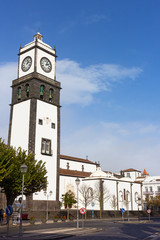 Fototapeta premium St. Sebastian Church tower with bells and clock in Ponta Delgada on Sao Miguel Island in Azores, Portugal. The Main Church of the city and surrounding buildings on a sunny winter day.