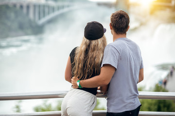 Happy tourist couple enjoying the view to Niagara Falls during romantic vacation. People looking to...