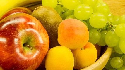 Naklejka na ściany i meble Obstschale - Aprikosen, Äpfel, Kiwi und Weintrauben in einer Holzschale
