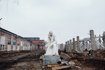 Damaged Lenin statue sitting on a chair with  book in his hand.