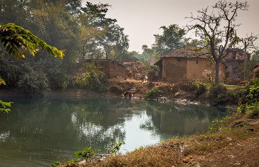 Fototapeta na wymiar A village pond with ducks surrounded with mud houses. Rural beauty of an Indian village in Bankura, West Bengal.