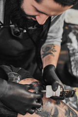 Fototapeta na wymiar Tattoo master in black gloves, tattoo on the skin of black ink tattoo of his client in the salon.