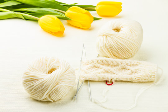roll of white soft knitting yarn, knitting mittens and yellow tu