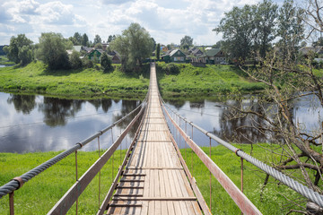Fototapeta premium Znikająca stara, długa, wisząca drewniana kładka z szynami nad rzeką. Wieś Koegoscha, obwód nowogrodzki, Rosja.