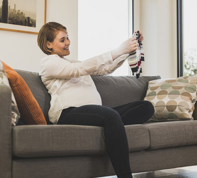 Pregnant woman on couch holding baby clothes