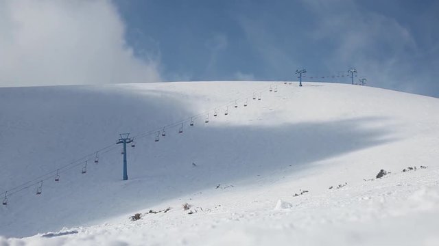 Ski resort with empty alpine skiing tracks and stopped ski lift. Large shadows of clouds are running over white smooth snow slopes.