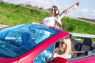 Two beautiful young women sitting in the car and enjoy.Colored and under exposed photo