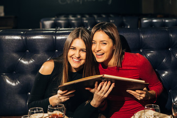 two young beautiful women sitting in a restaurant with menu and laugh