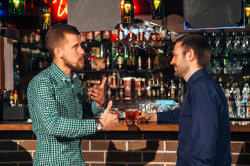two young man talking at counter.  friends standing in bar and drinking whisky