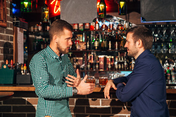 two young man talking at counter.  friends standing in bar and drinking whisky