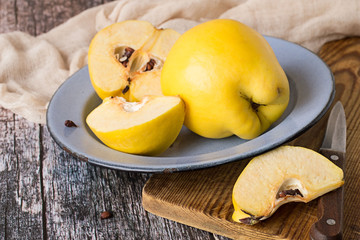  Fresh fruits. Blue metal plate with fruits of quince, whole and cut into slices, cutting board, knife and napkin on old wooden table.