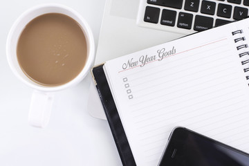 A note book with New Year Goals word and computer, smart phone,