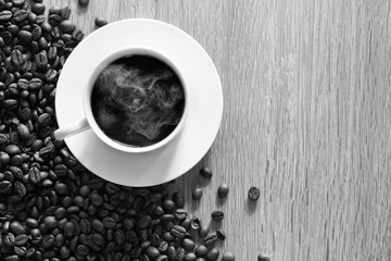 White coffee cup and pile of coffee seeds on brown wooden plate / Top view and Select focus image, Space for text, black and white
