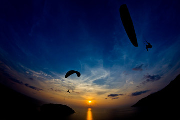Paraglide silhouettes flying above the sea against colorful sunset background. Promthep Cape, Phuket, Thailand.