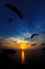 Paraglide silhouettes flying above the sea against colorful sunset background. Promthep Cape, Phuket, Thailand.