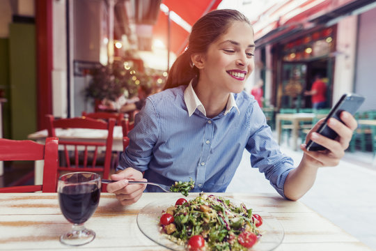 beautiful young woman using an application to send an sms message in her smartphone device while eating a salad