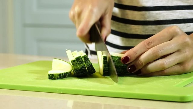 Cooking ratatouille. Female hands cutting zucchini into slices on plastic cutting board. HD
