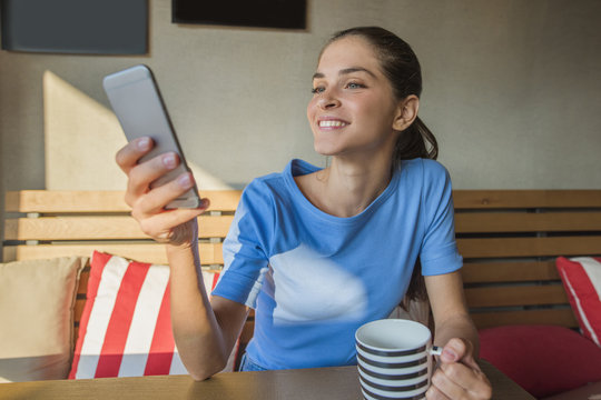 a woman is using an app in her smart phone device while indoors at cafe restaurant and holding a beverage