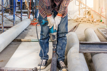 Worker using electric screwdriver for fixing steel construction frames on construction site.