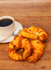 Coffee and croissant for breakfast on rustic wooden table, top view