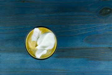 Overhead view of whipped cream on cup of coffee with blue wood table in background