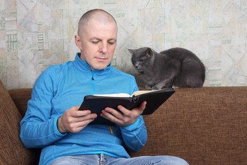 man sitting on sofa and reading a book of the Bible