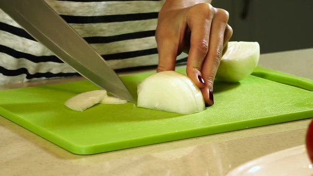Cooking ratatouille. Female hands cutting onion into slices on plastic cutting board. HD