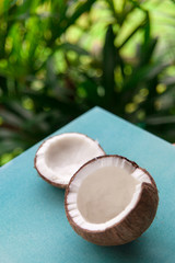 Still life of ripe tropical fruit on a bright blue surface on green nature background. Coconut cut into two halves.