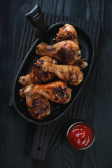 Frying pan with bbq chicken legs over black wooden background