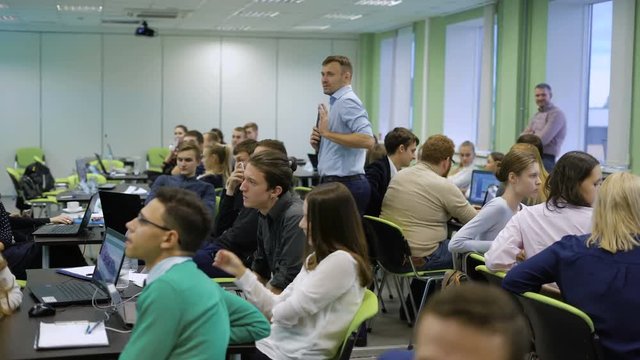 Speaker with microphone and large group of people are waiting for the results of teambuilding contest.