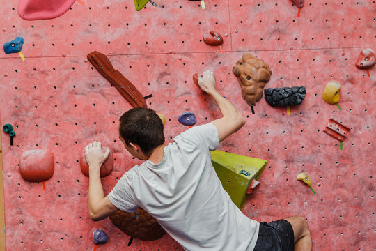 Free climber young man climbing artificial boulder indoors, back view