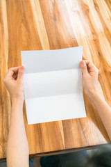 Obraz premium Women hand hold Trifold white template paper on wood texture .