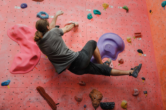 Young man professional climber exercising at indoor bouldering artificial wall