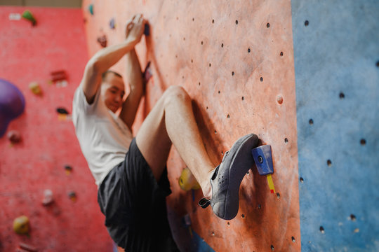Rear view of a young man practicing in climbing at artificial wall in gym