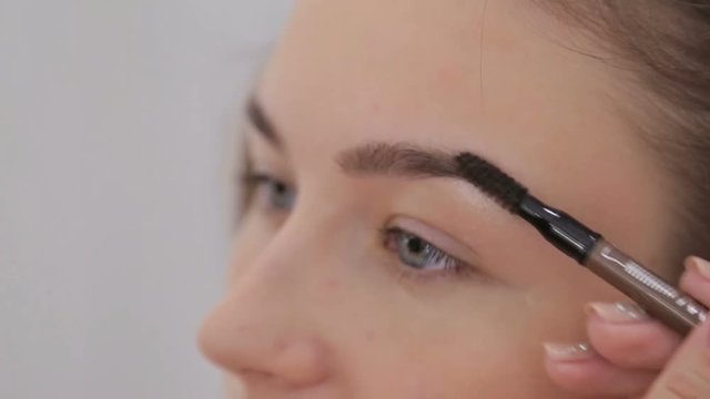 Close up shot. Professional make-up artist drawing eyebrows of client in white room. Beauty, makeup and fashion concept