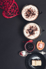 Romantic breakfast. Two Cups of coffee, cappuccino with chocolate cookies and biscuits near red hearts on black table background. Valentine day. Love. Top view.