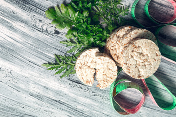 Pieces of crispbread near measuring tape and green arugula on grey background. Diet concept. Healthy food. Top view. Copy space. Frame.