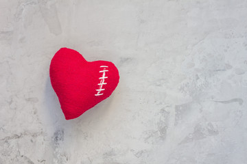 Handmade textile heart was broken and sewed again with white thread on gray concrete background